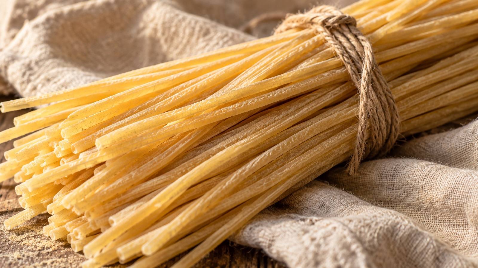 Un mazzo di pasta lunga legato con lo spago, su un telo di lino